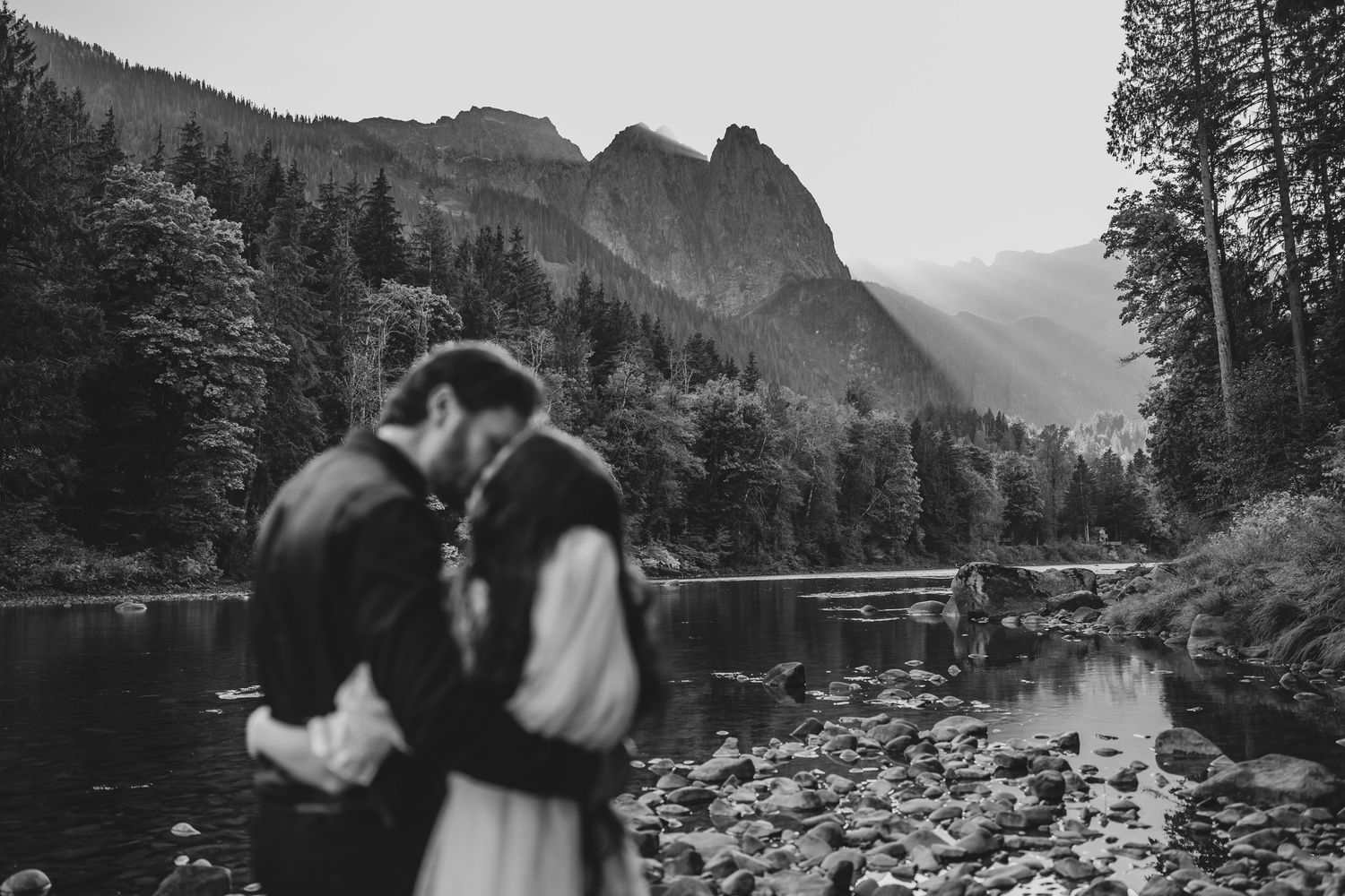 Black and white romantic portrait by a lake with mountain peaks in the background.