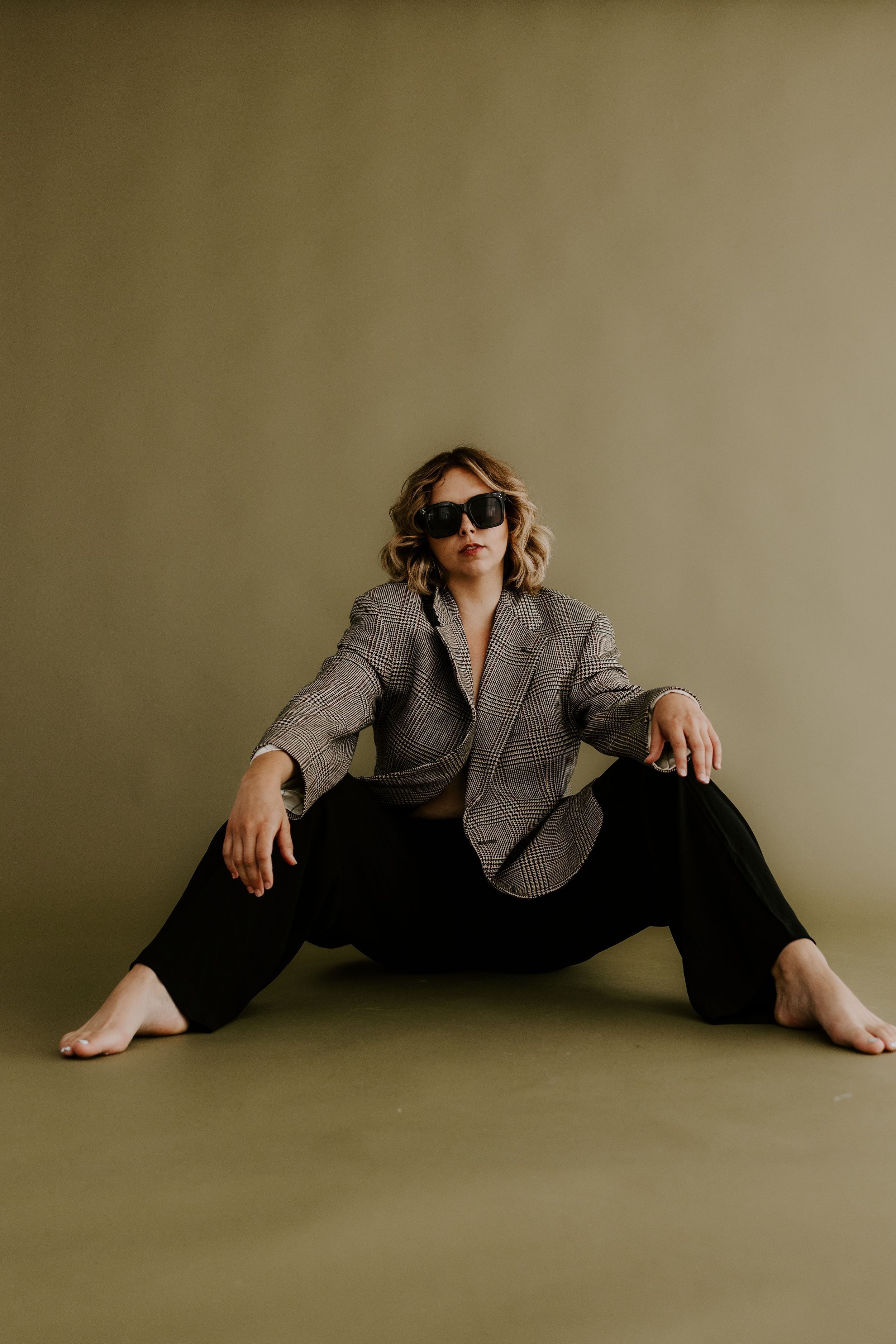 Fashion portrait with plaid blazer and sunglasses against beige backdrop.