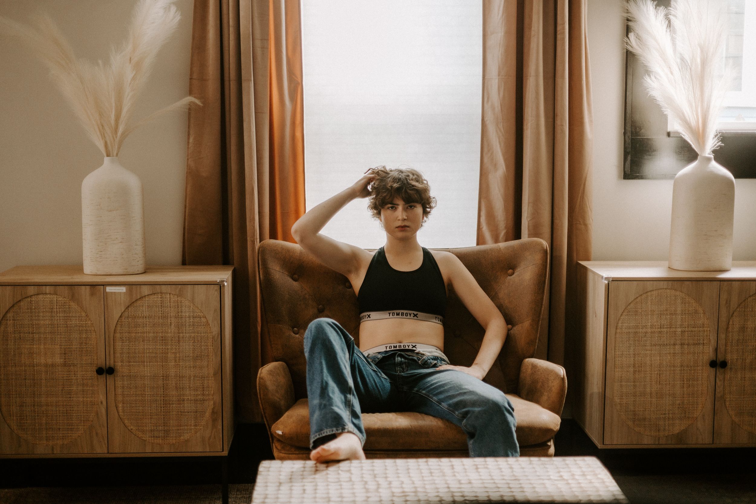 Lifestyle photo of person relaxing in tan armchair near window with decorative vases.