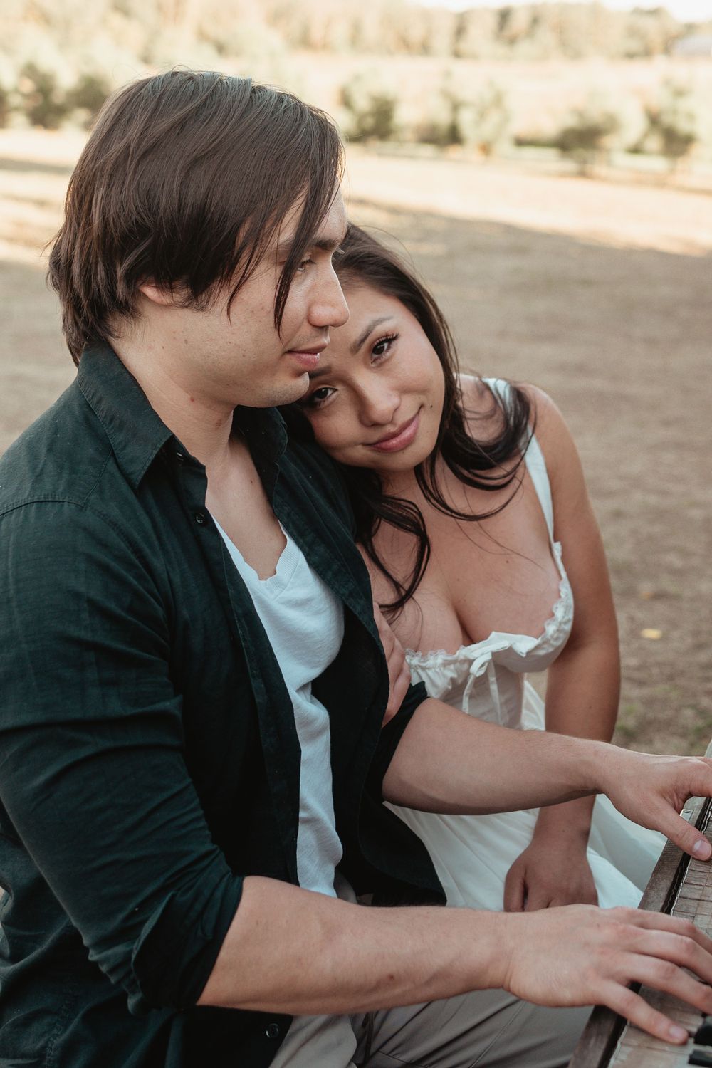 A romantic outdoor portrait of a couple sitting close together in golden hour lighting.