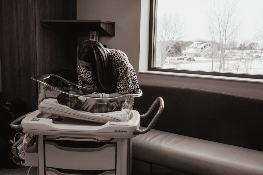 Person in patterned sweater reads while sitting by window in winter, creating cozy monochromatic scene.