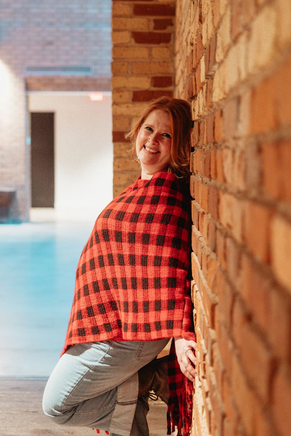 Person wearing red plaid wrap leaning against rustic brick wall with outdoor lighting.