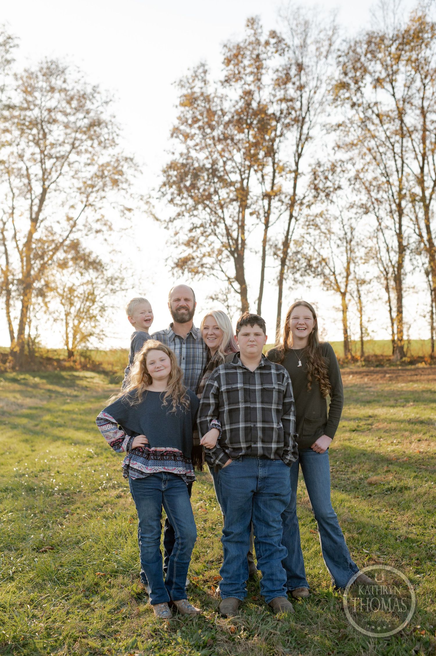 A group poses together outdoors at sunset with tall autumn trees in the background.