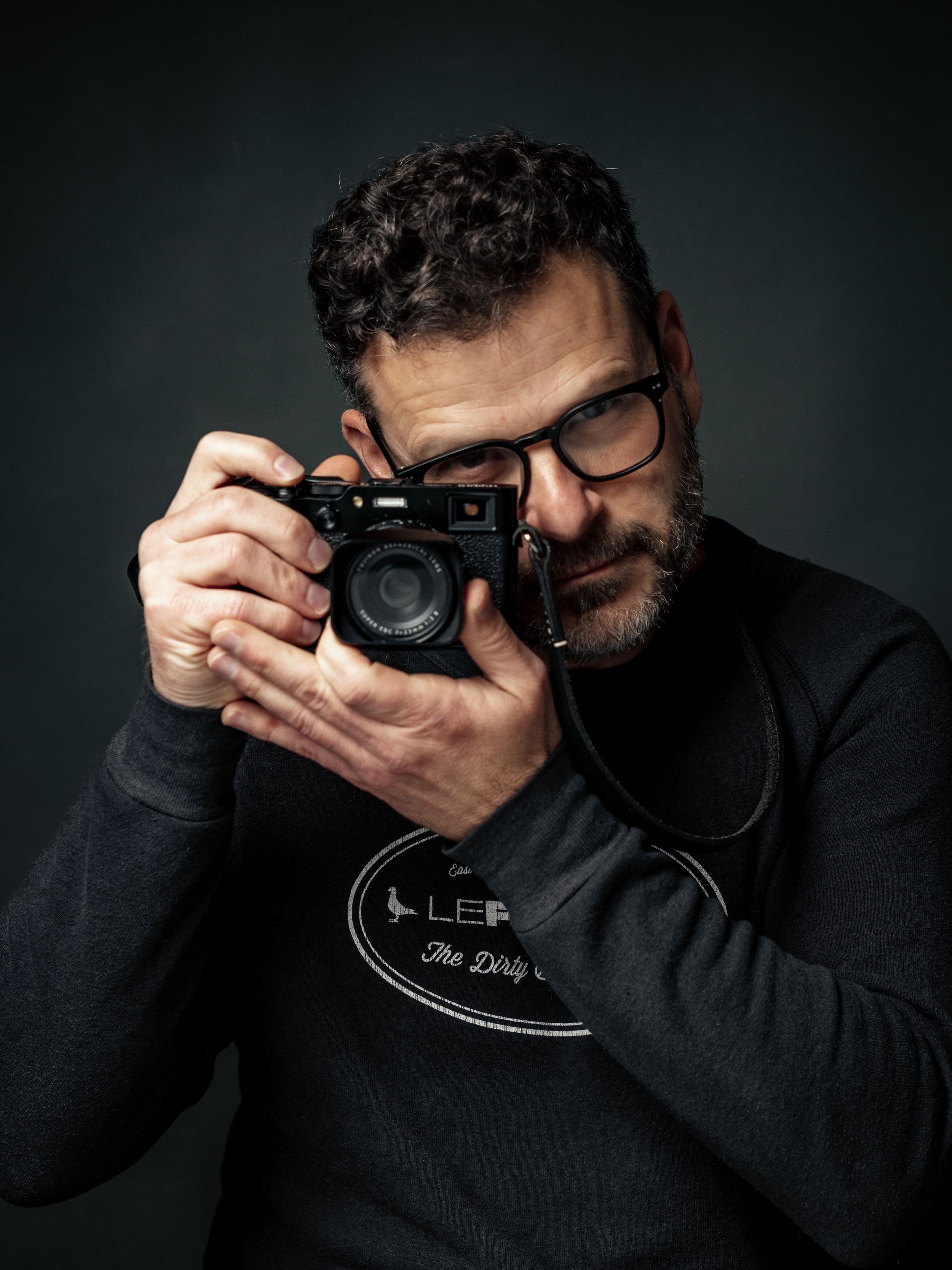 Close-up photo of photographer holding vintage camera against dark background. Dustin Pattison