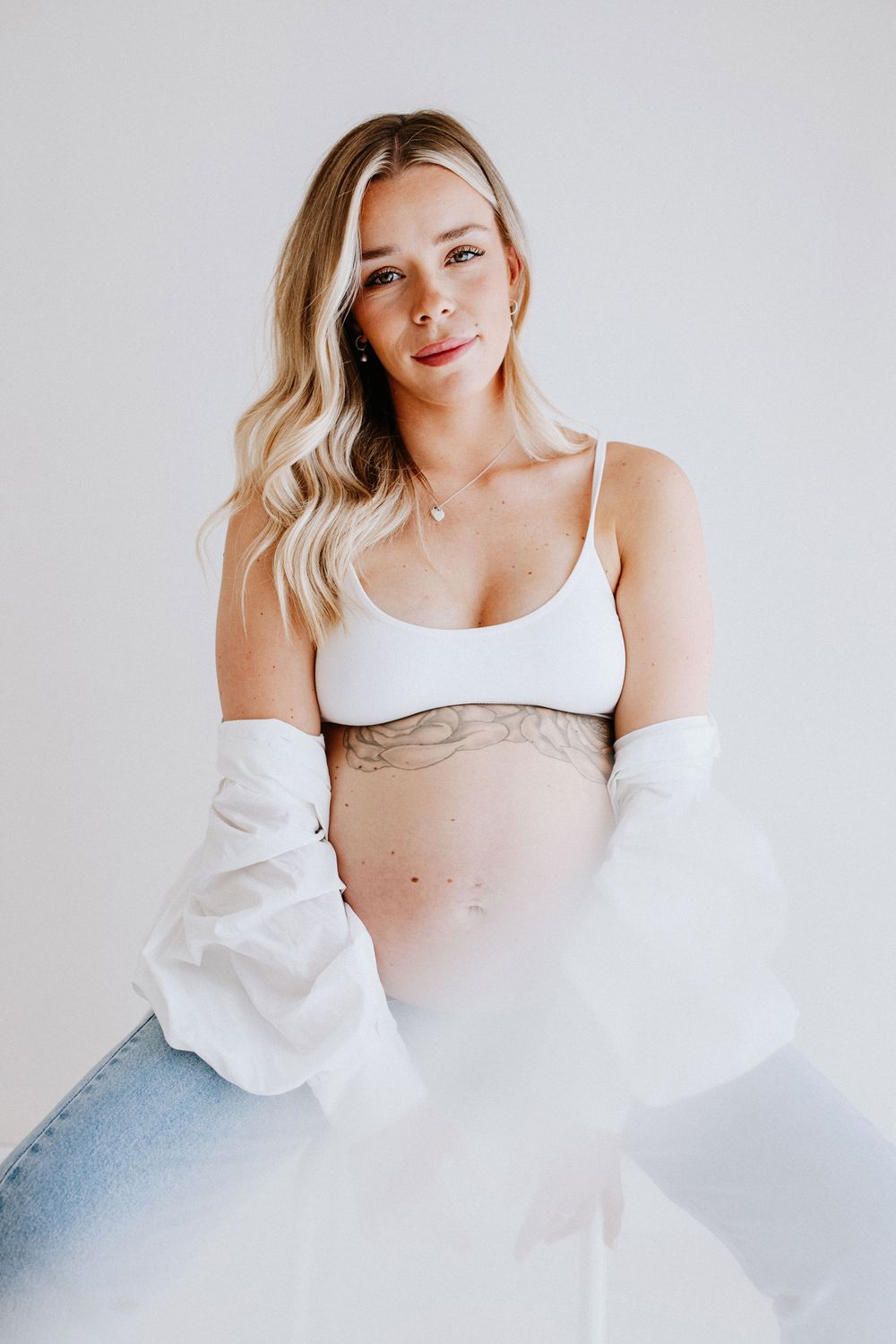 A soft, ethereal maternity portrait featuring flowing white fabric and casual denim.
