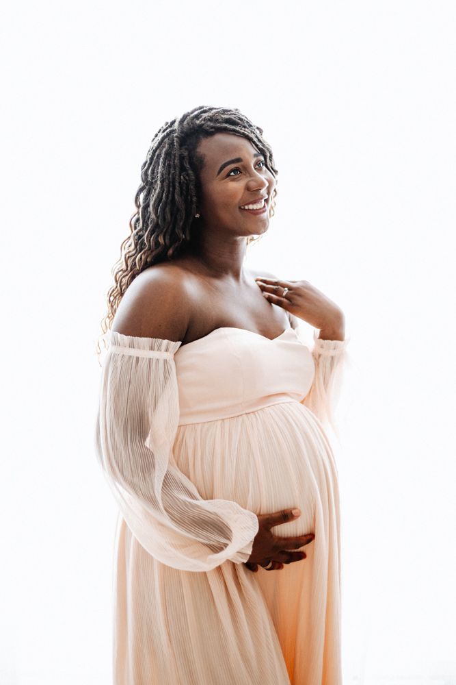 A person in a flowing off-shoulder white dress poses elegantly against a bright white background.