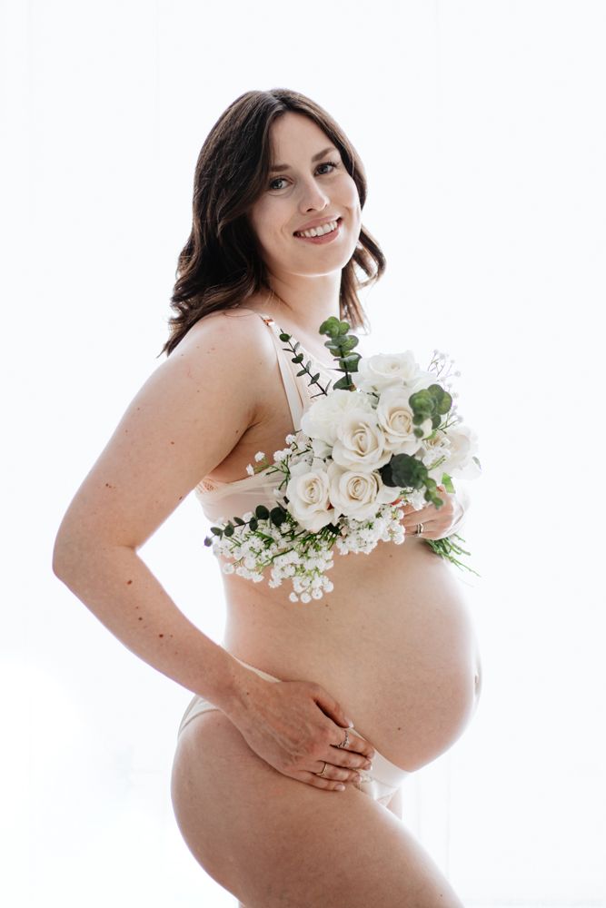Artistic backlit maternity photo with mother holding white roses and baby's breath bouquet against her bump.