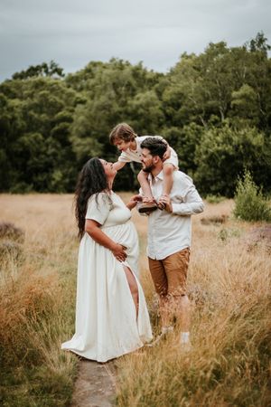 A couple stands together with their toddler in a golden field during sunset, surrounded by trees during maternity photoshoot in Nottingham