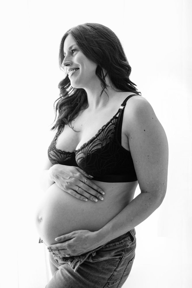 Black and white maternity portrait showing expectant mother in lingerie smiling at her partner off camera while holding her belly.