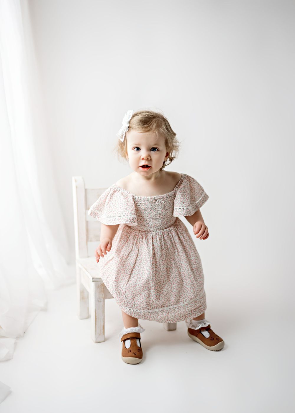 A small child in a delicate floral dress and brown shoes stands against a white background in three similar poses.