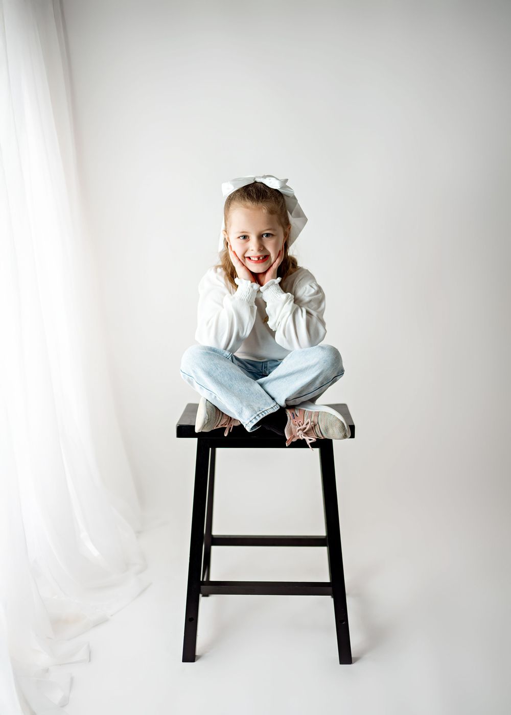 Three sequential photos show a small child in light clothing expressing joyful emotions while sitting on a black stool.
