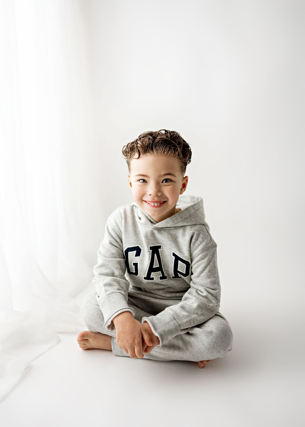 A child in a gray Gap sweatshirt poses on a white backdrop in a series of casual studio portraits.