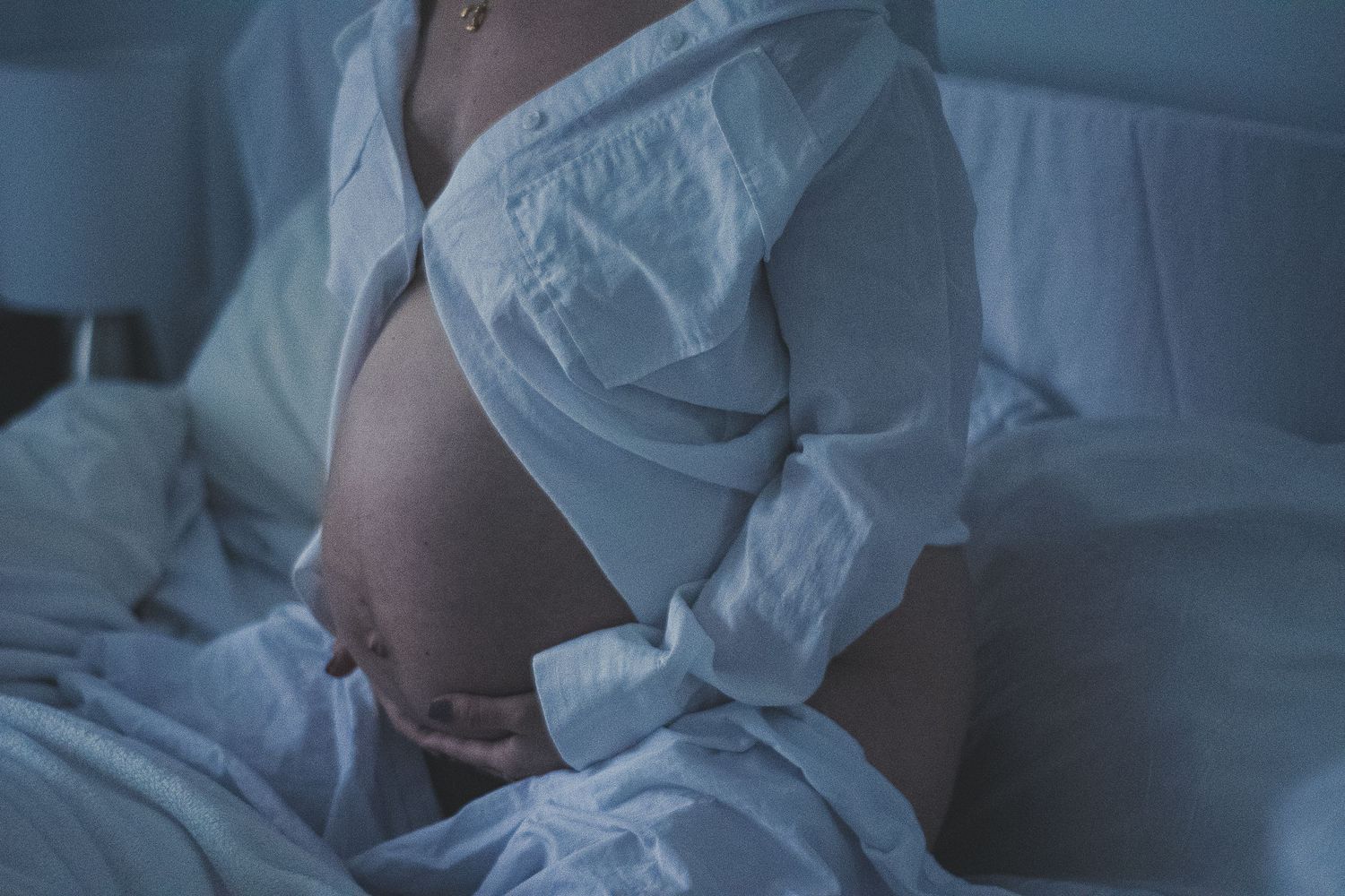 A side view of a pregnant belly in soft lighting while lying on white bedding.