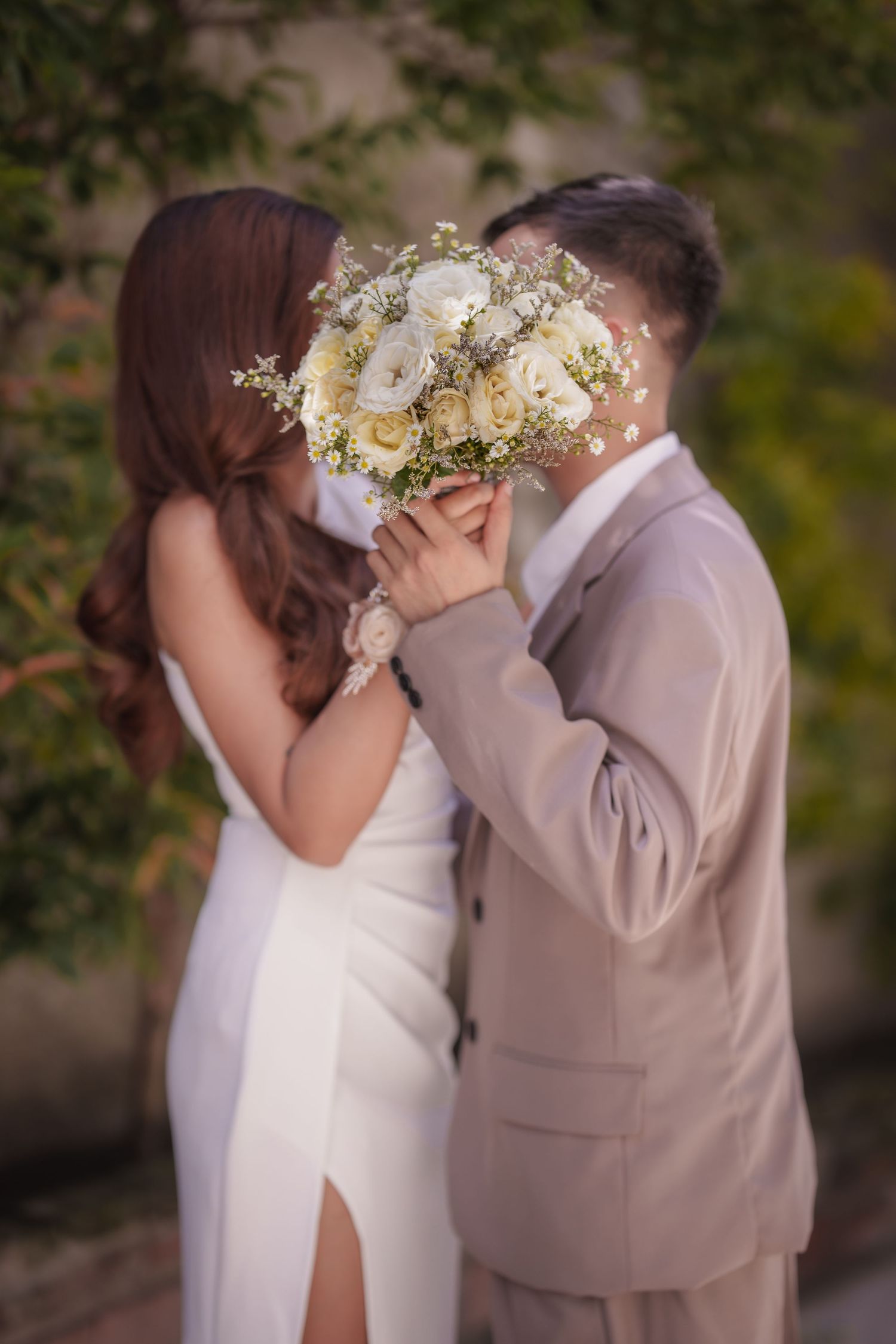 Romantic wedding photo with couple kissing behind white floral bouquet in outdoor setting.