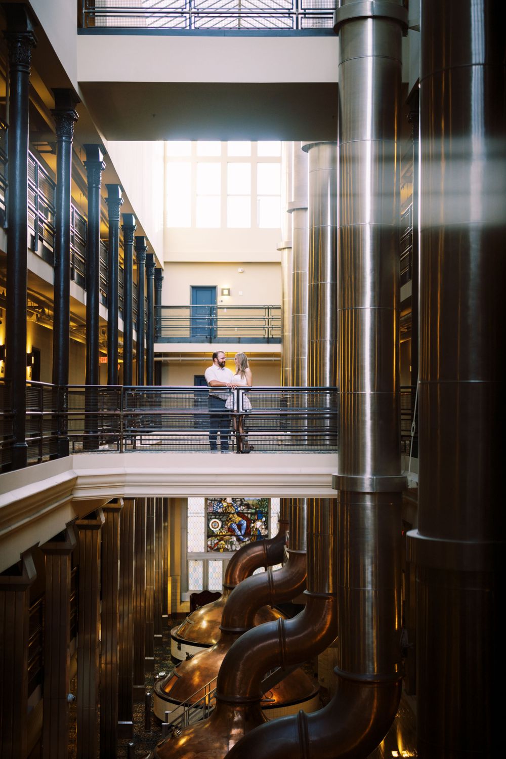 Interior of a multi-level industrial space with metal railings and large brass machinery visible below.