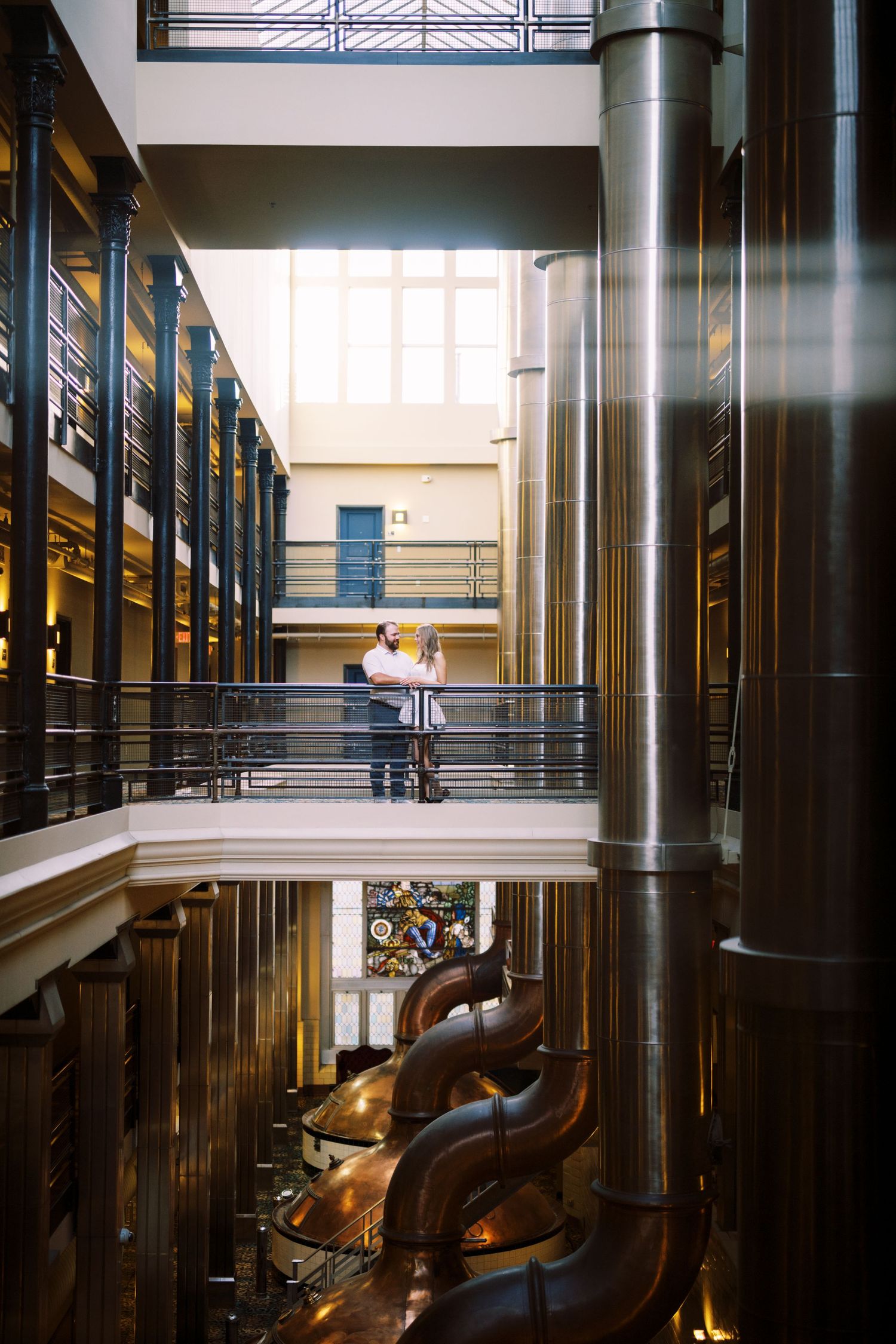 Interior of a multi-level industrial space with metal railings and large brass machinery visible below.