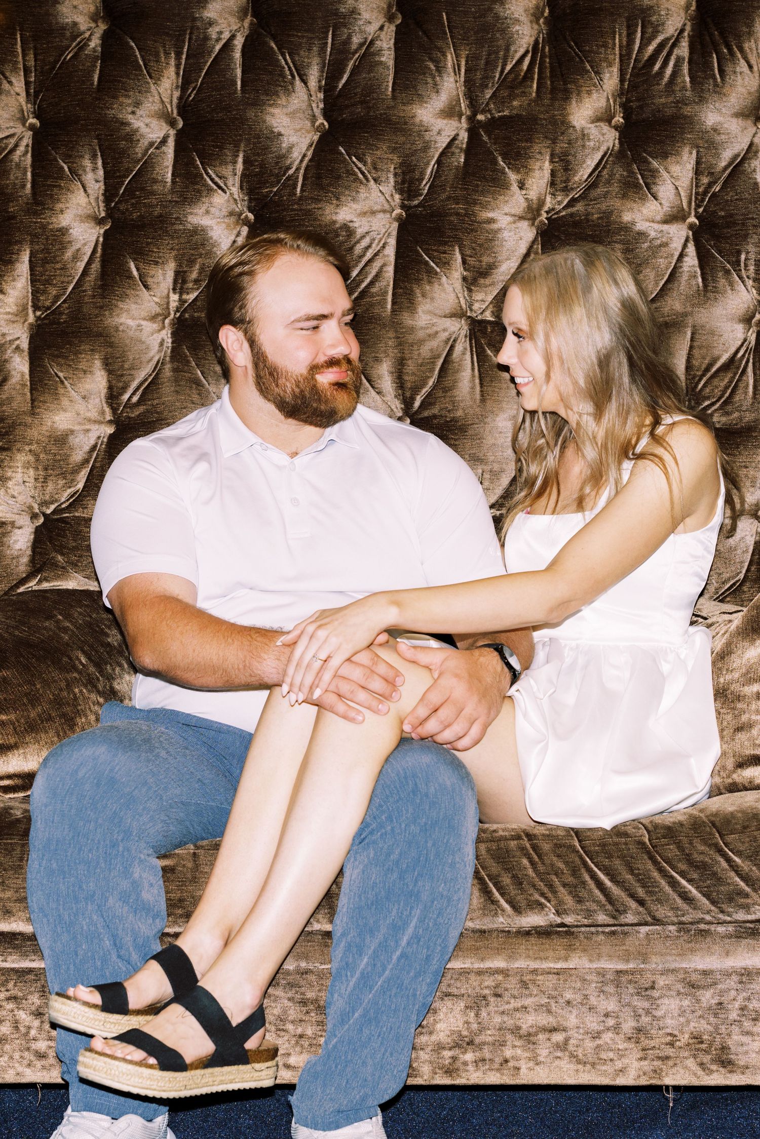 A couple share an intimate moment while sitting together on a tufted velvet couch.
