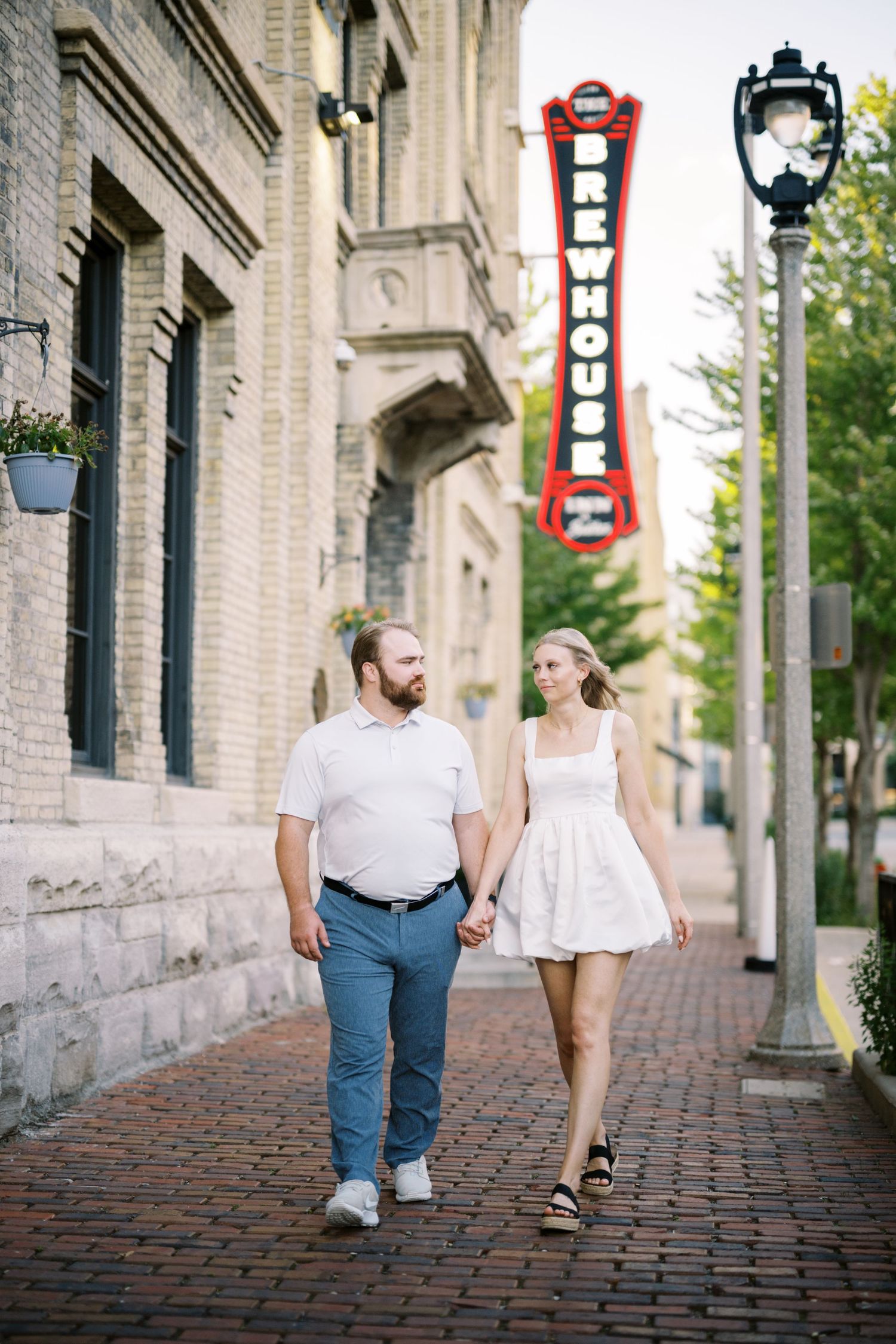 A couple strolls along a brick sidewalk past historic buildings with a vintage Brewhouse sign visible above.