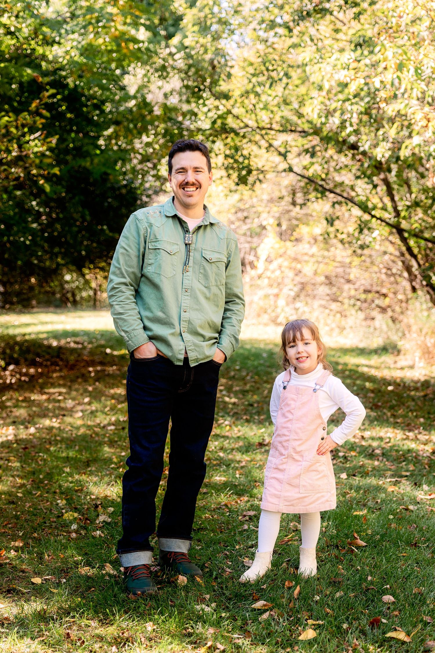 Dad and daughter pose for a portrait in a sunlit autumn park with golden foliage in the background. Novi Northville Michigan