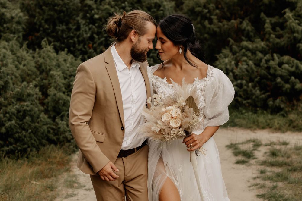 A romantic wedding portrait featuring a floral bouquet and elegant bridal gown outdoors.