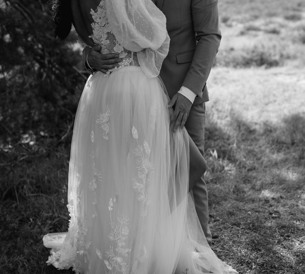 A detailed view of a delicate lace wedding dress with flowing fabric against a natural backdrop.