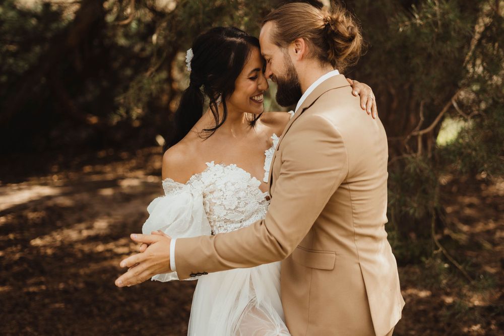 A sun-drenched wedding portrait showing a tender embrace in a forest setting.