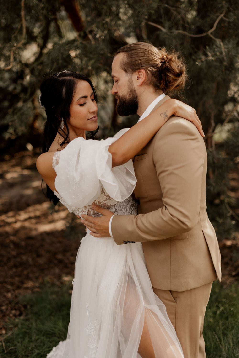 A romantic wedding portrait in warm tones showing an intimate embrace in a wooded setting.