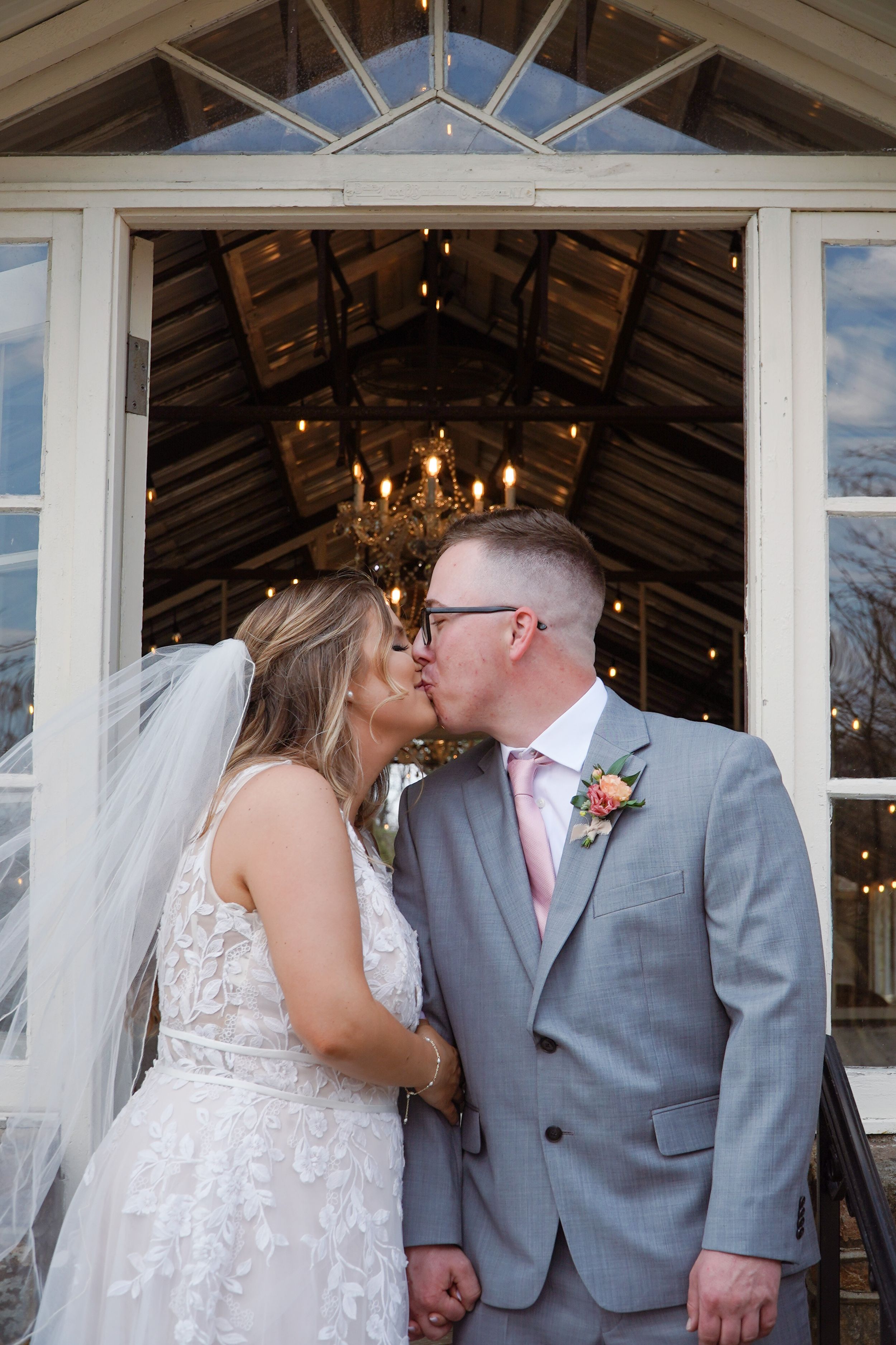 A romantic moment captured inside a rustic venue with vaulted ceilings and chandeliers during a wedding ceremony.