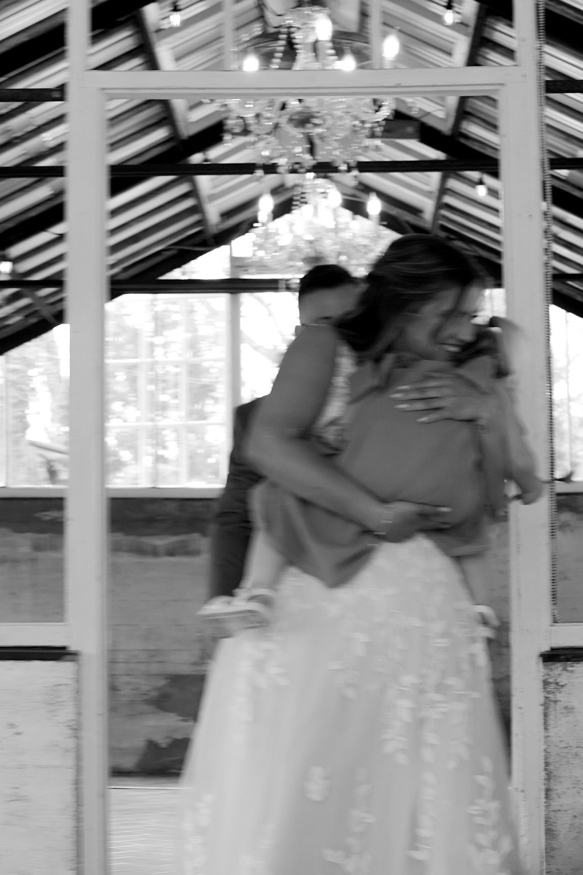 A romantic black and white moment captured under a decorative gazebo with a chandelier overhead.