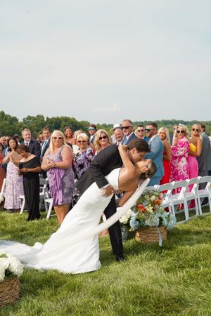 Romantic dip kiss during outdoor wedding ceremony with guests watching.