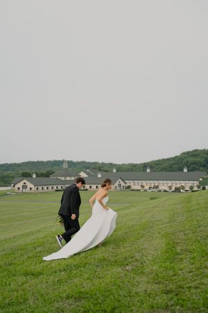Wedding couple walks on a scenic hilltop with buildings and rolling hills in the background.