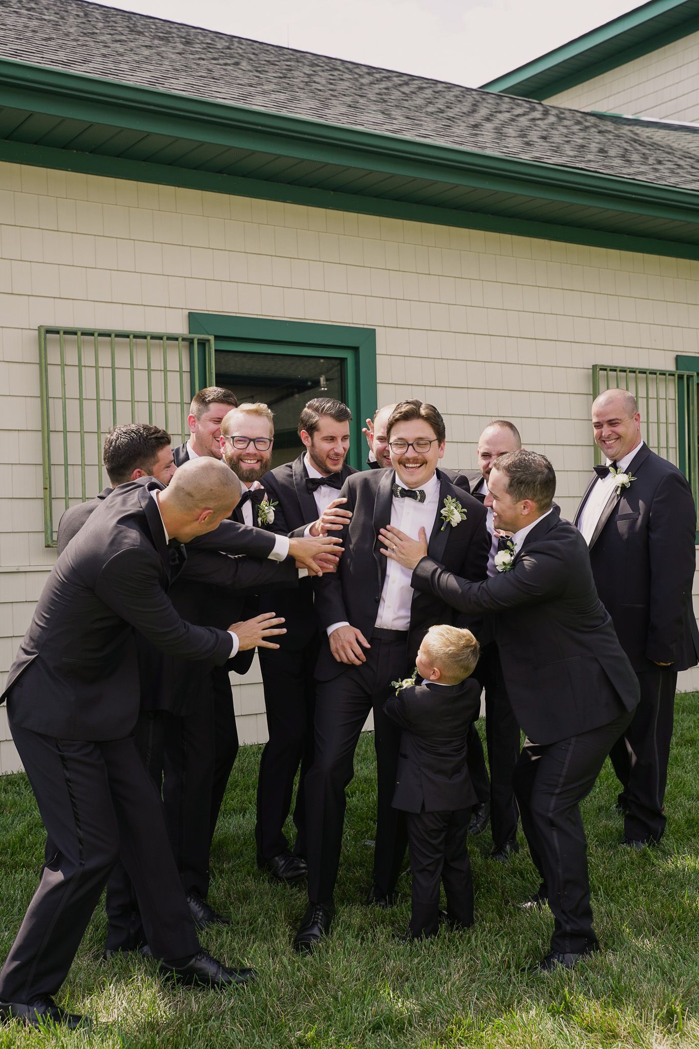 Groomsmen share laughs and drinks during casual outdoor wedding photo.
