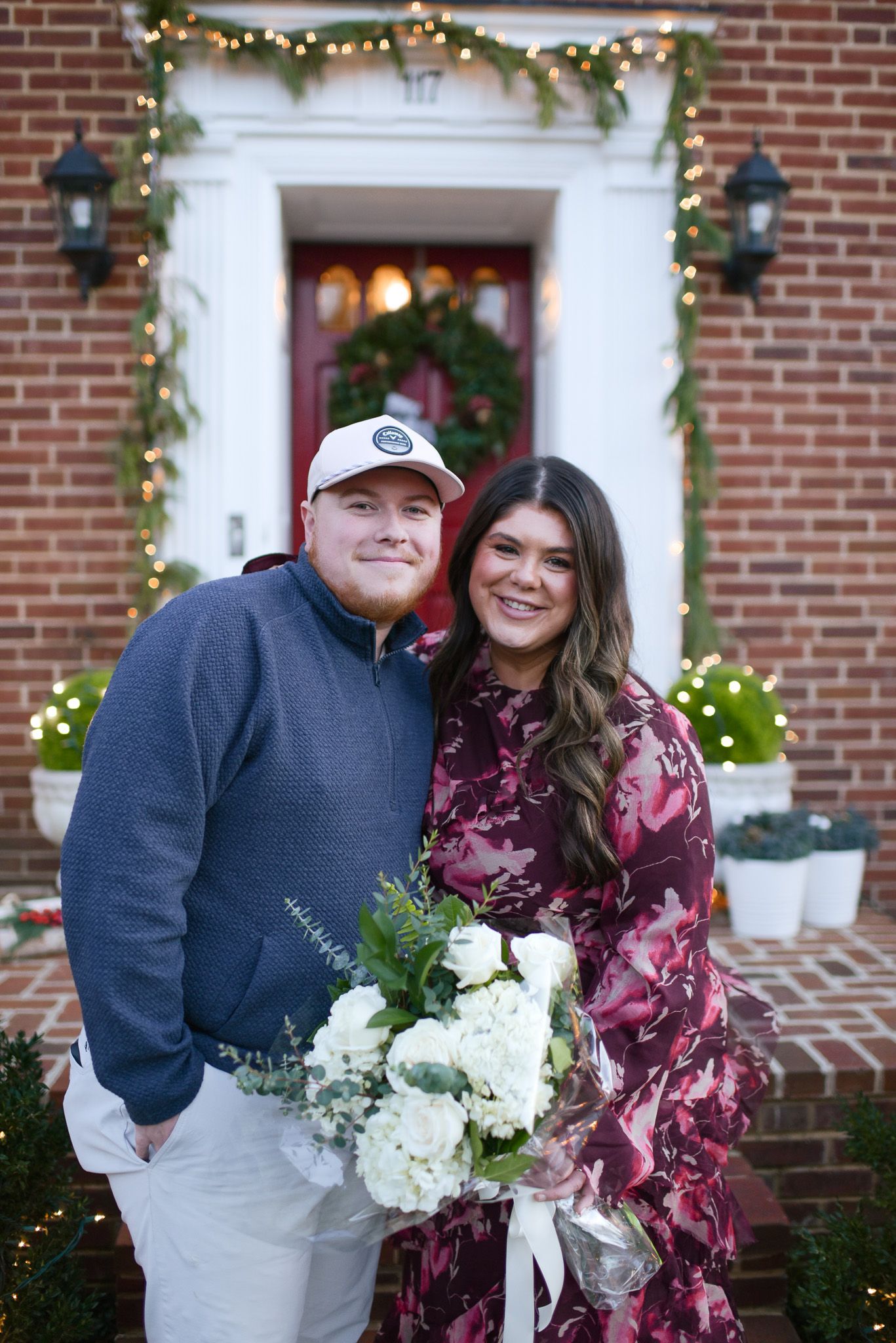 A festive holiday entrance with a wreath and greenery garland lit by string lights.