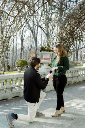 A romantic proposal moment captured on a stone terrace surrounded by winter trees and white railings.