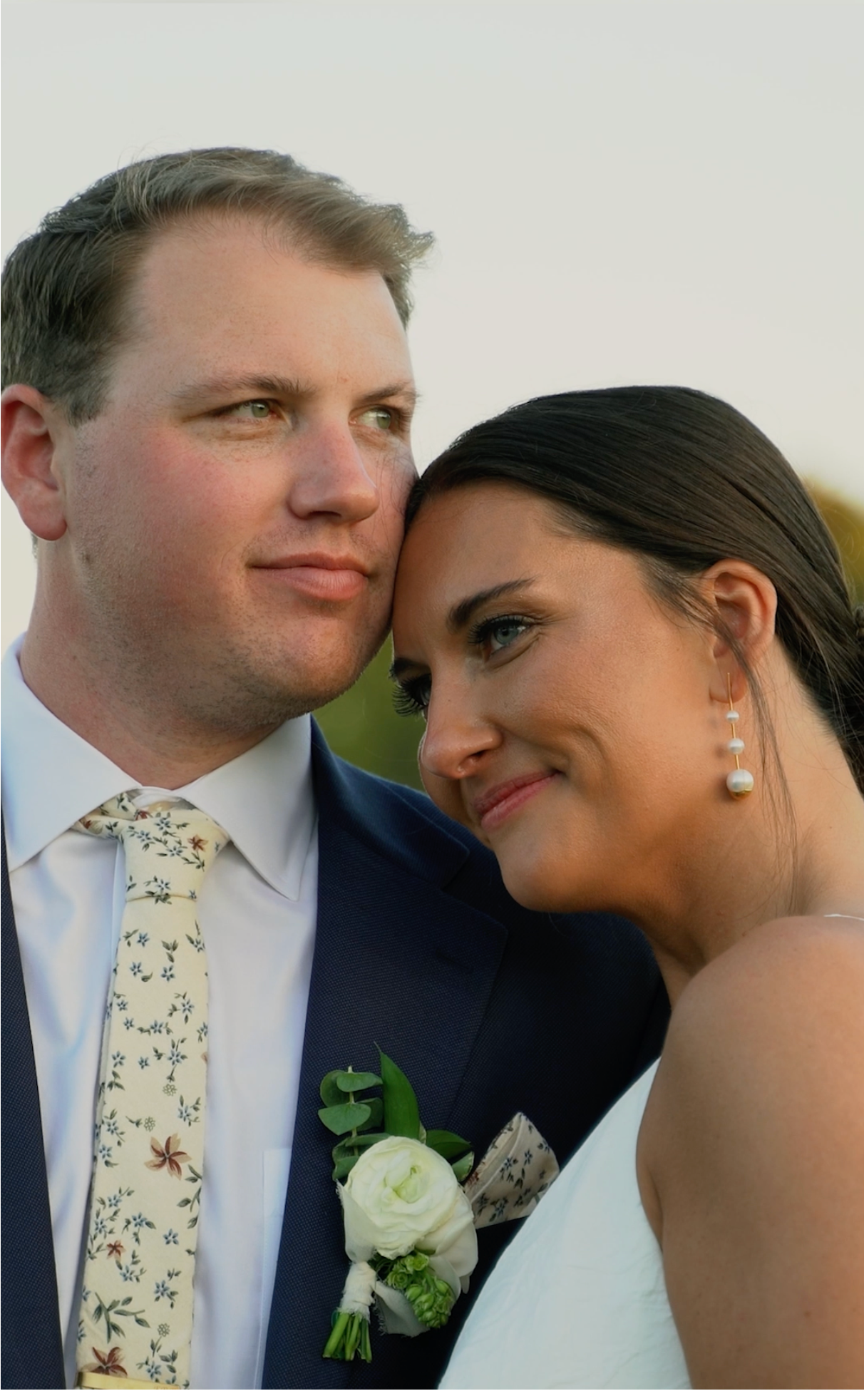 Close-up portrait of newlyweds in elegant wedding attire with a floral boutonniere.