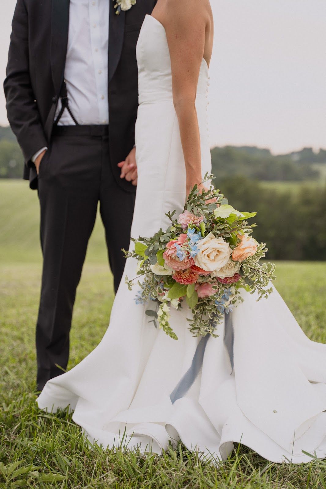 Close-up of bride and groom with lush pastel bouquet featuring roses and greenery.