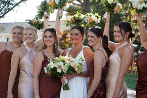 Wedding party poses under floral arch wearing burgundy and neutral dresses.