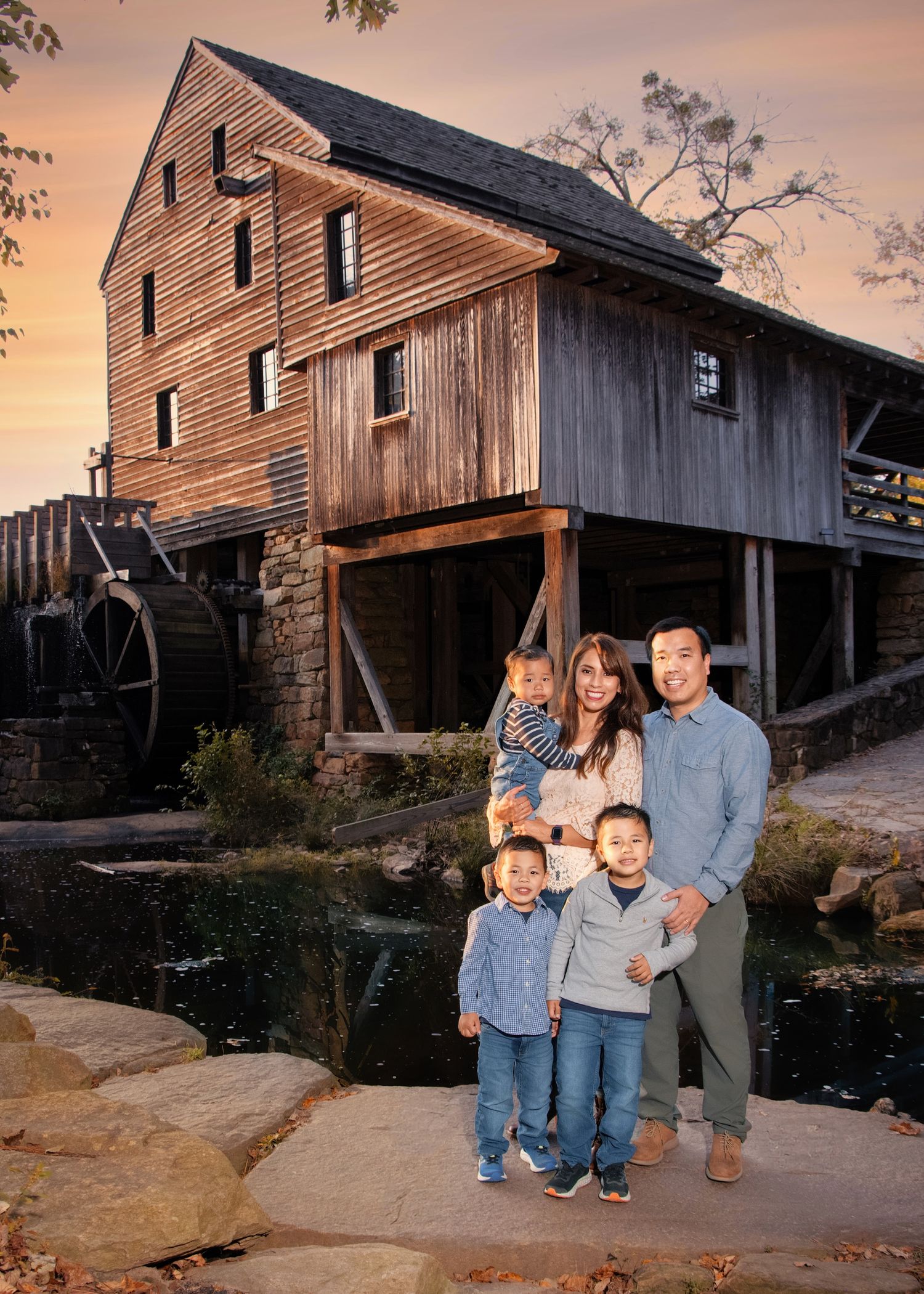 A family portrait in front of a rustic wooden mill at sunset.