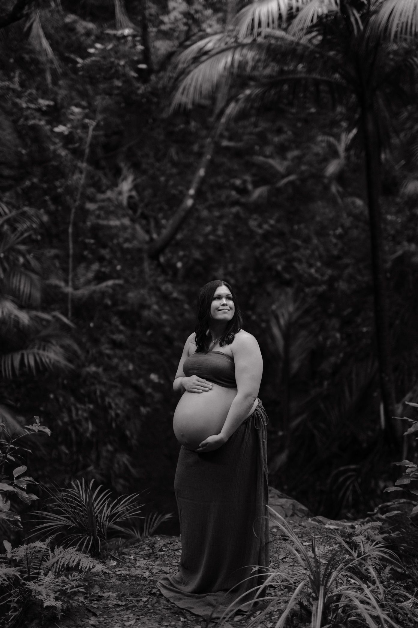 A black and white photo of someone standing in a lush tropical garden with palm fronds in the background.