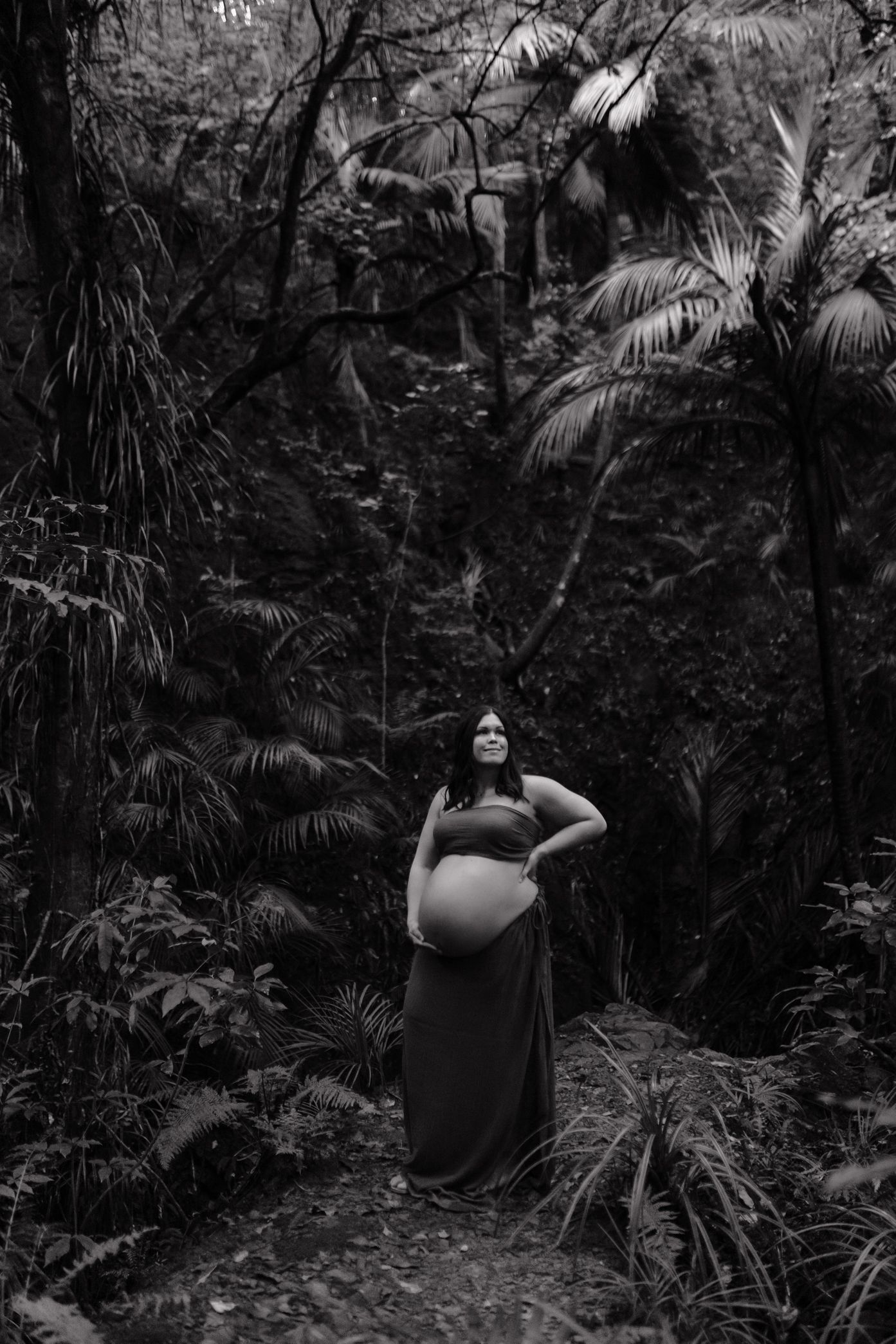 A figure in dark clothing walks through a dense tropical forest path surrounded by palm fronds and lush vegetation.