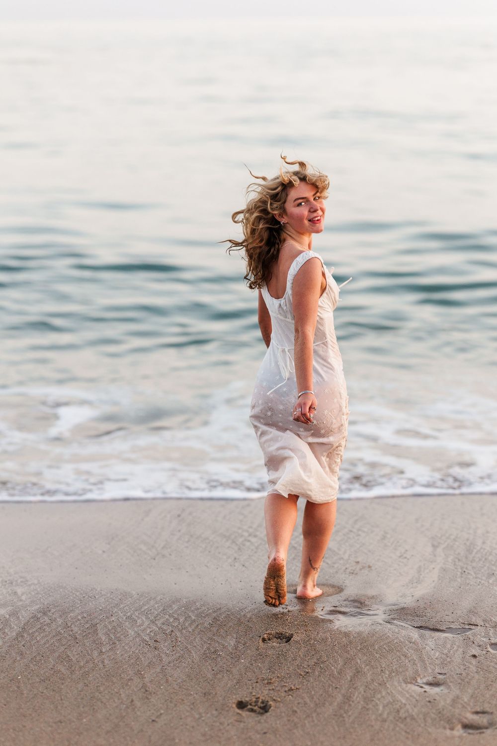 A joyful moment captured as someone in a flowing white dress runs along the beach at sunset.