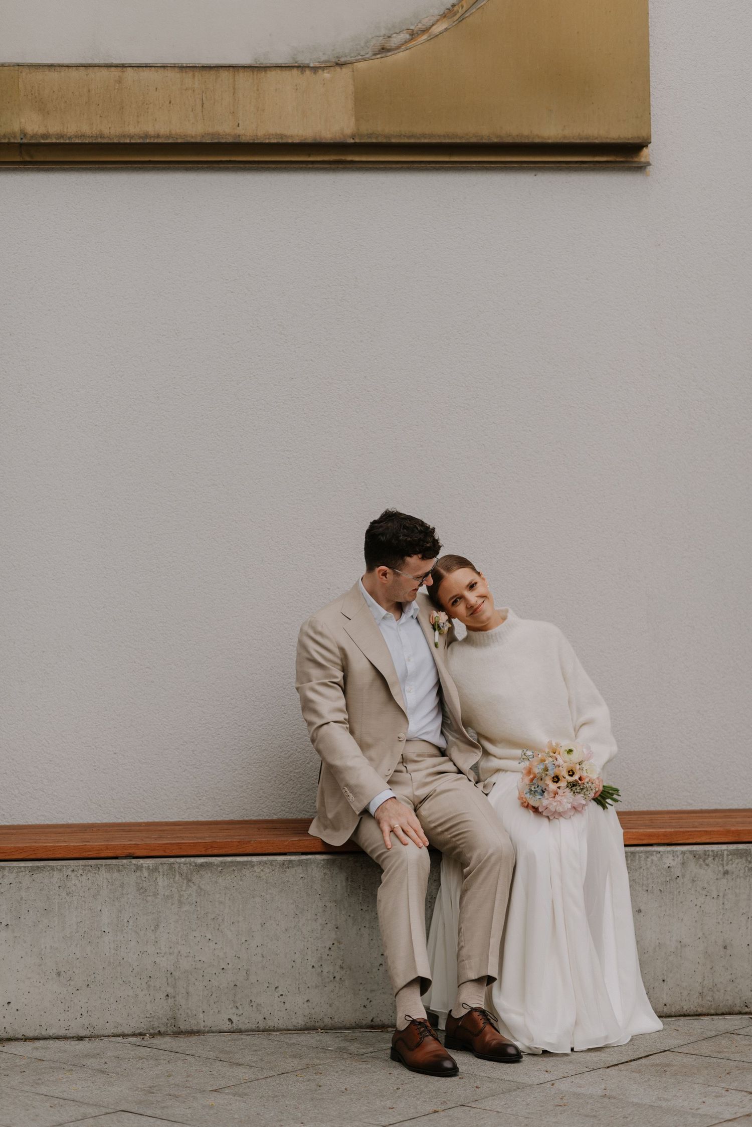 Minimalist wedding portraits of a couple in white and beige sitting together against neutral walls.