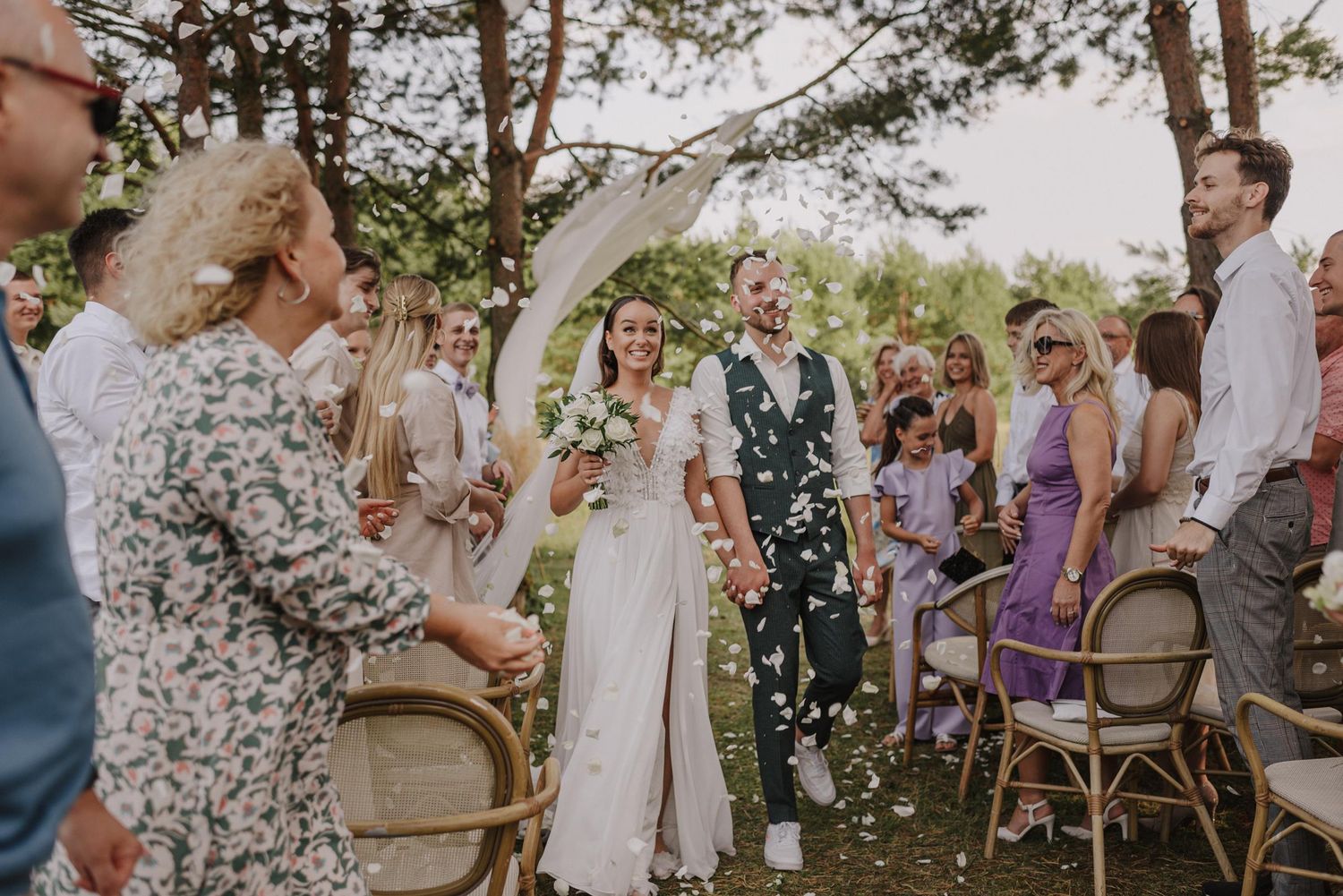 Outdoor wedding celebration with guests throwing confetti in a garden setting.