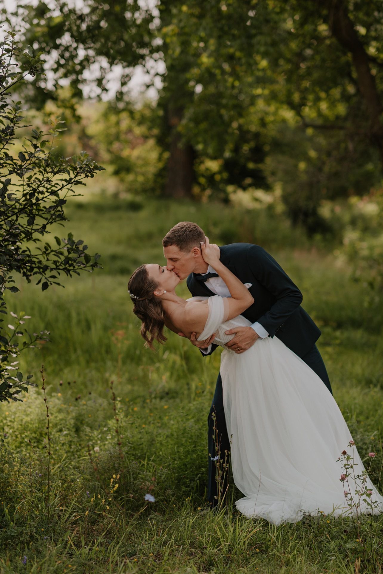 Romantic wedding photo of couple in white dress and suit dipping in a lush green garden setting.