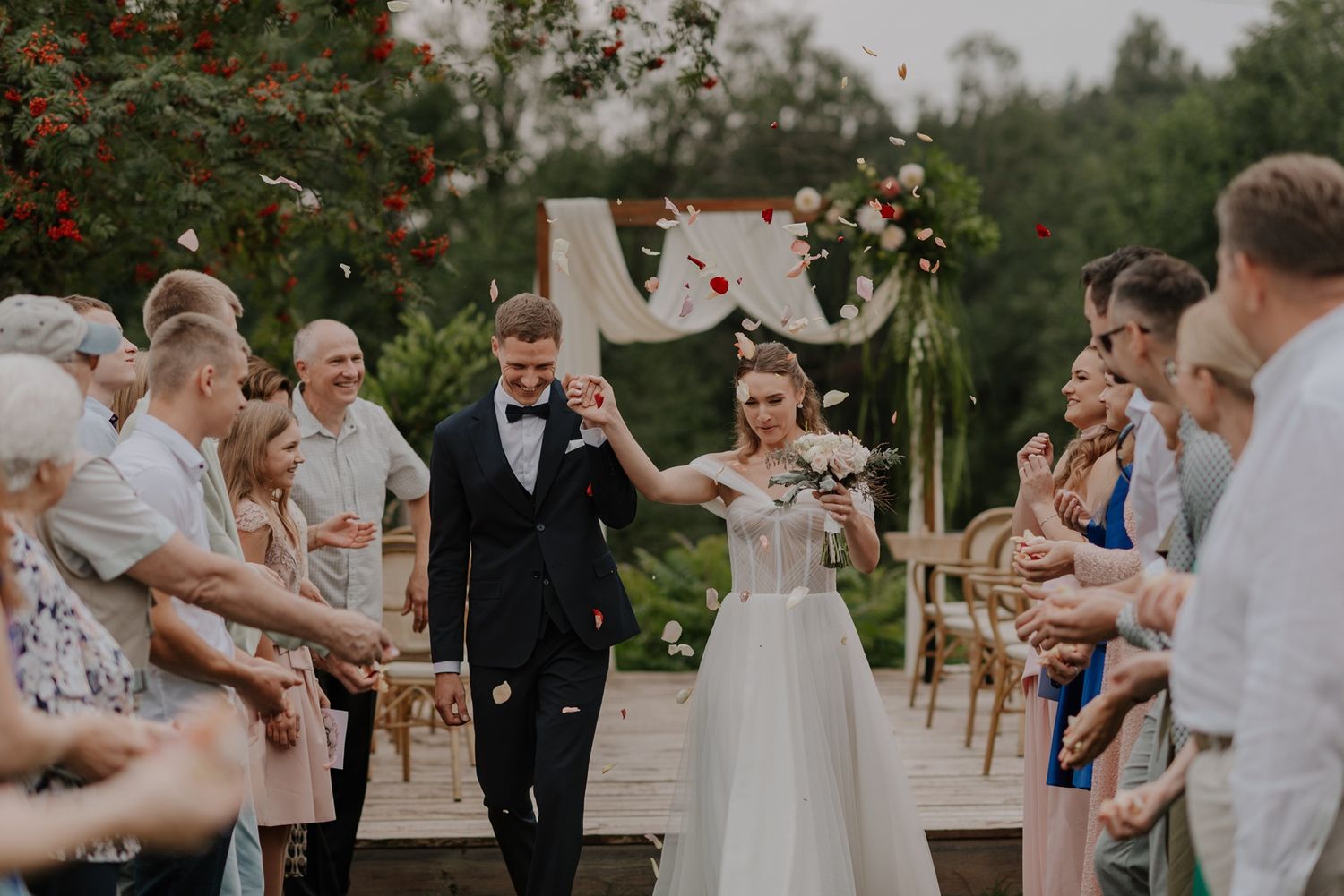 Happy newlyweds make their entrance at an outdoor wedding ceremony with guests clapping.