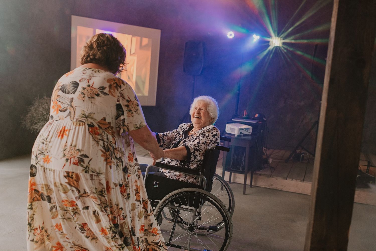 Wedding reception dance floor with purple lighting and people celebrating in the background.