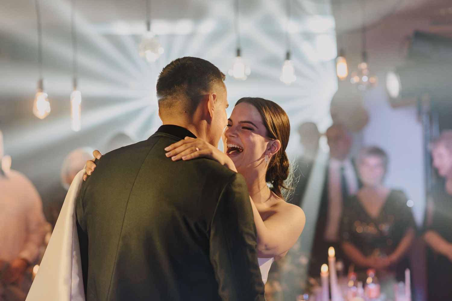 A romantic dance moment illuminated by soft overhead lighting at a wedding reception.