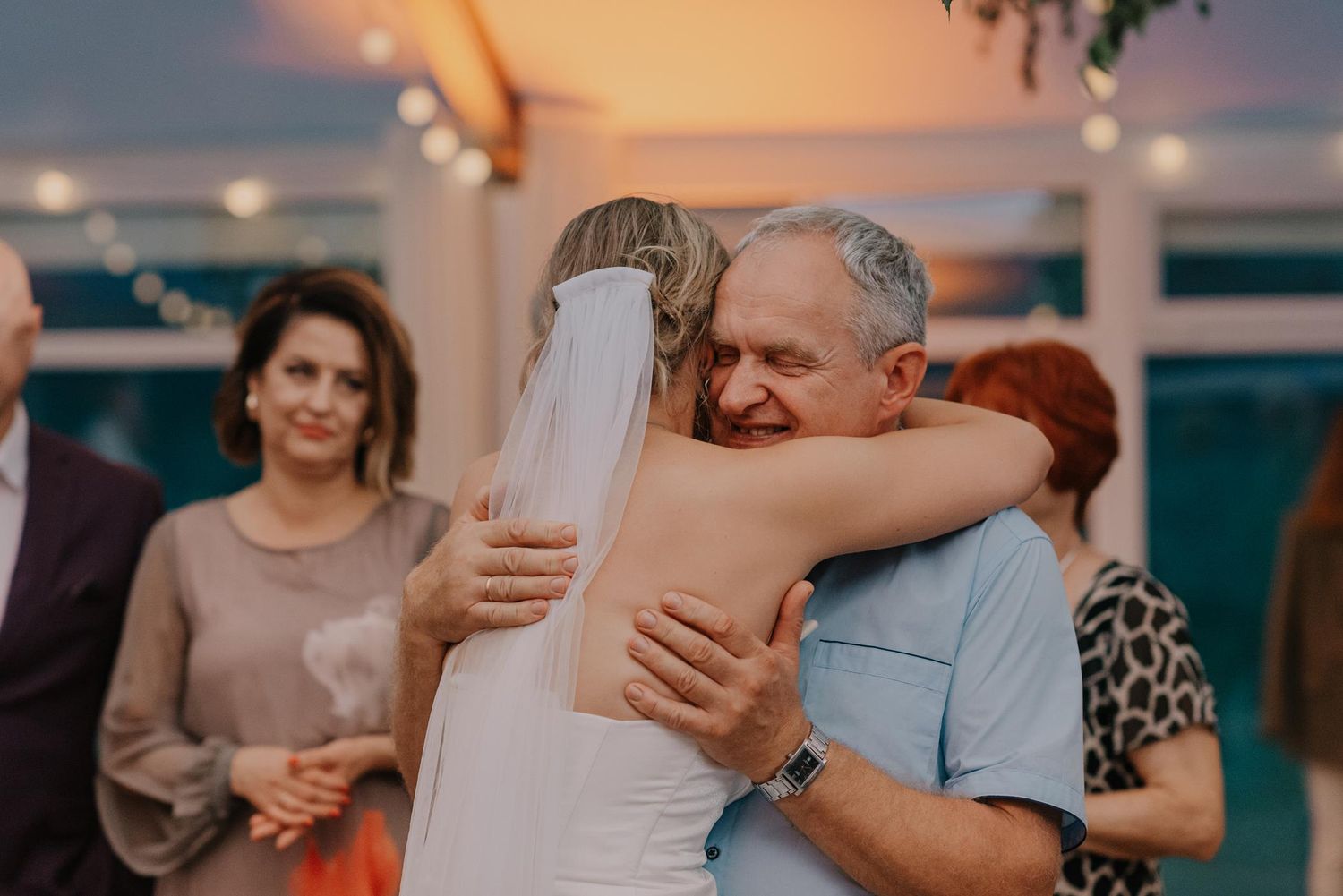 An emotional embrace during a wedding reception with warm sunset lighting.