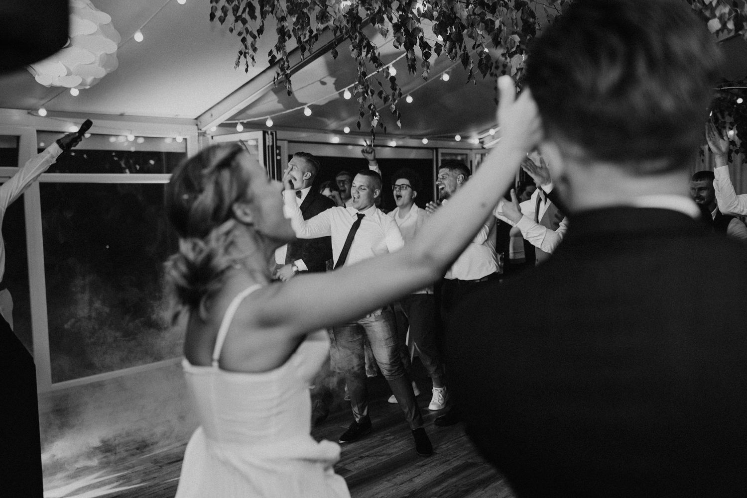 A black and white photo captures energetic dancing at a wedding reception.