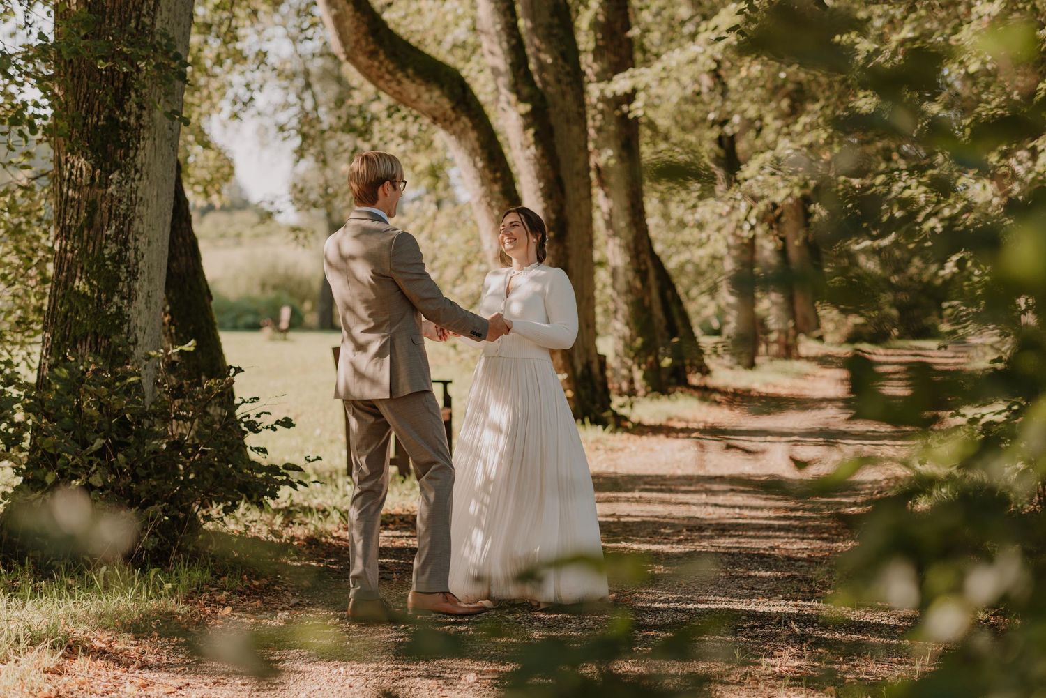 Sunlit wedding portraits captured on a serene garden pathway surrounded by trees.